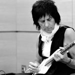 Jeff Beck, wearing a black vest, plays an electric guitar