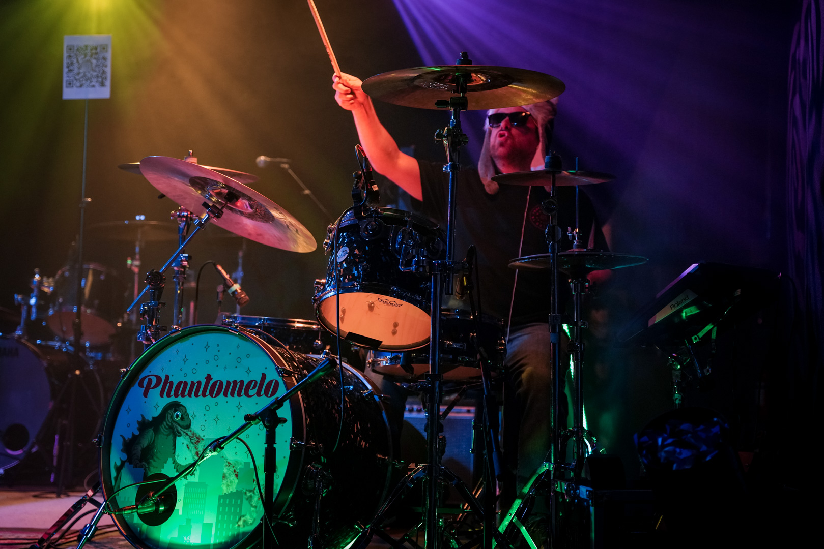 A drummer behind his drums playing with a drumstick in the hair in his right hand