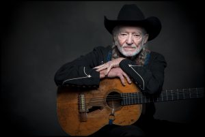 Willie Nelson, dressed in black, faces the camera with Trigger in his lap