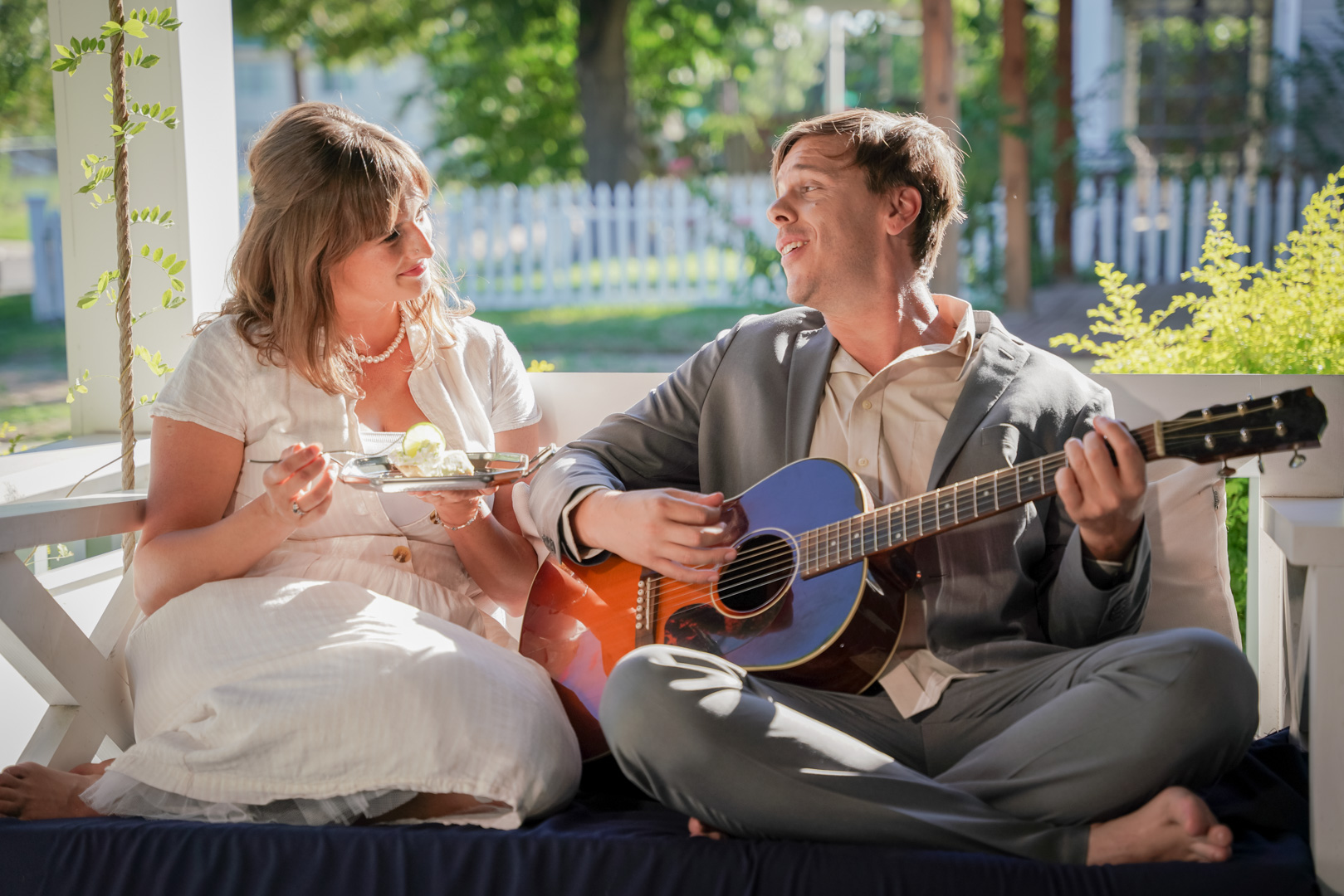 A woman and man istting on a porch swing, the man is playing guitar and singing to the woman