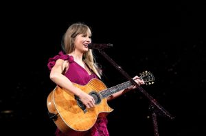 Taylor Swift, holding a guitar, sings to an audience