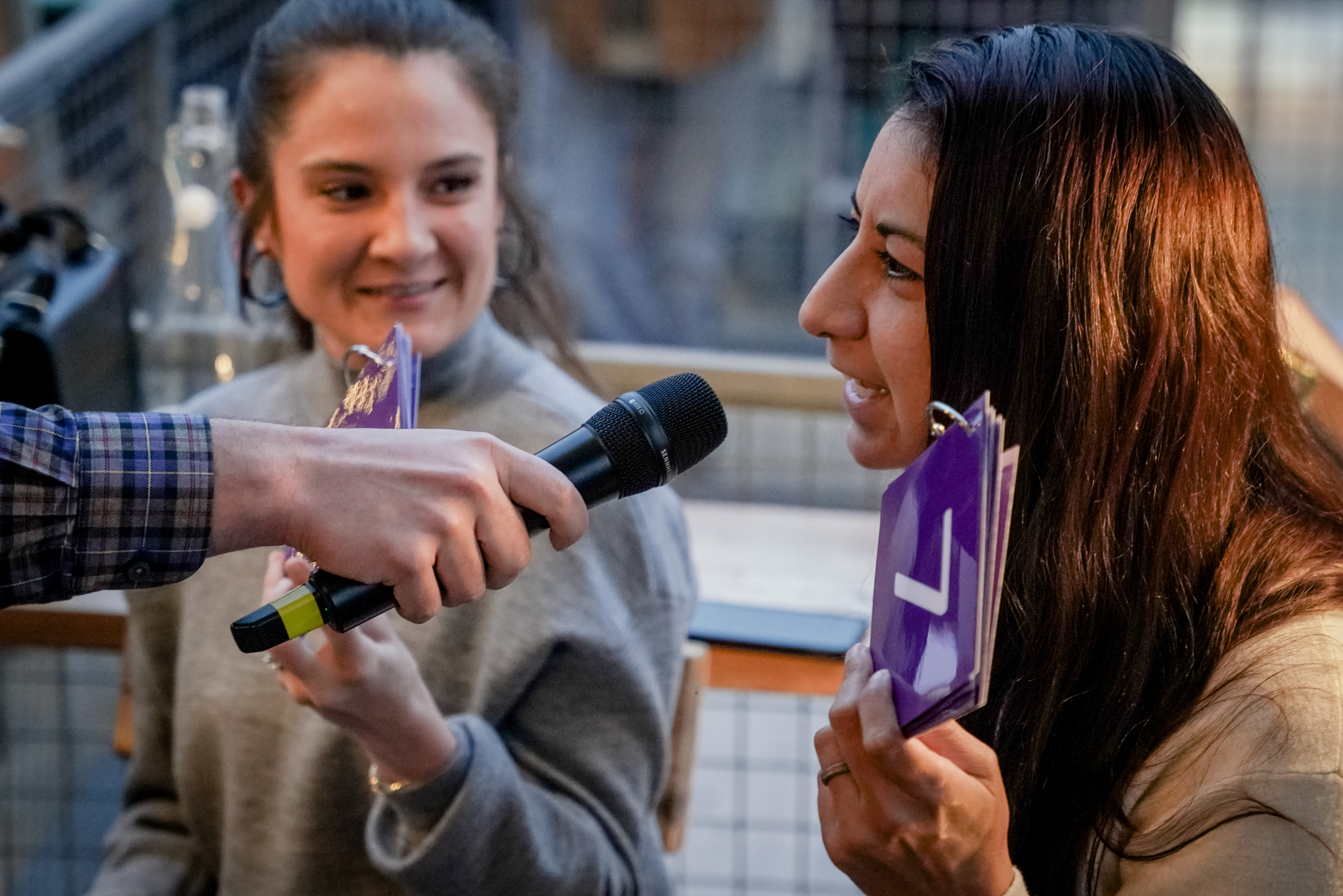 A woman speaking into a microphone, her friend smiling