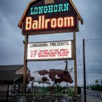 A huge neon-lit sign that looks like a barn house roof with a huge longhorn cattle sculpture