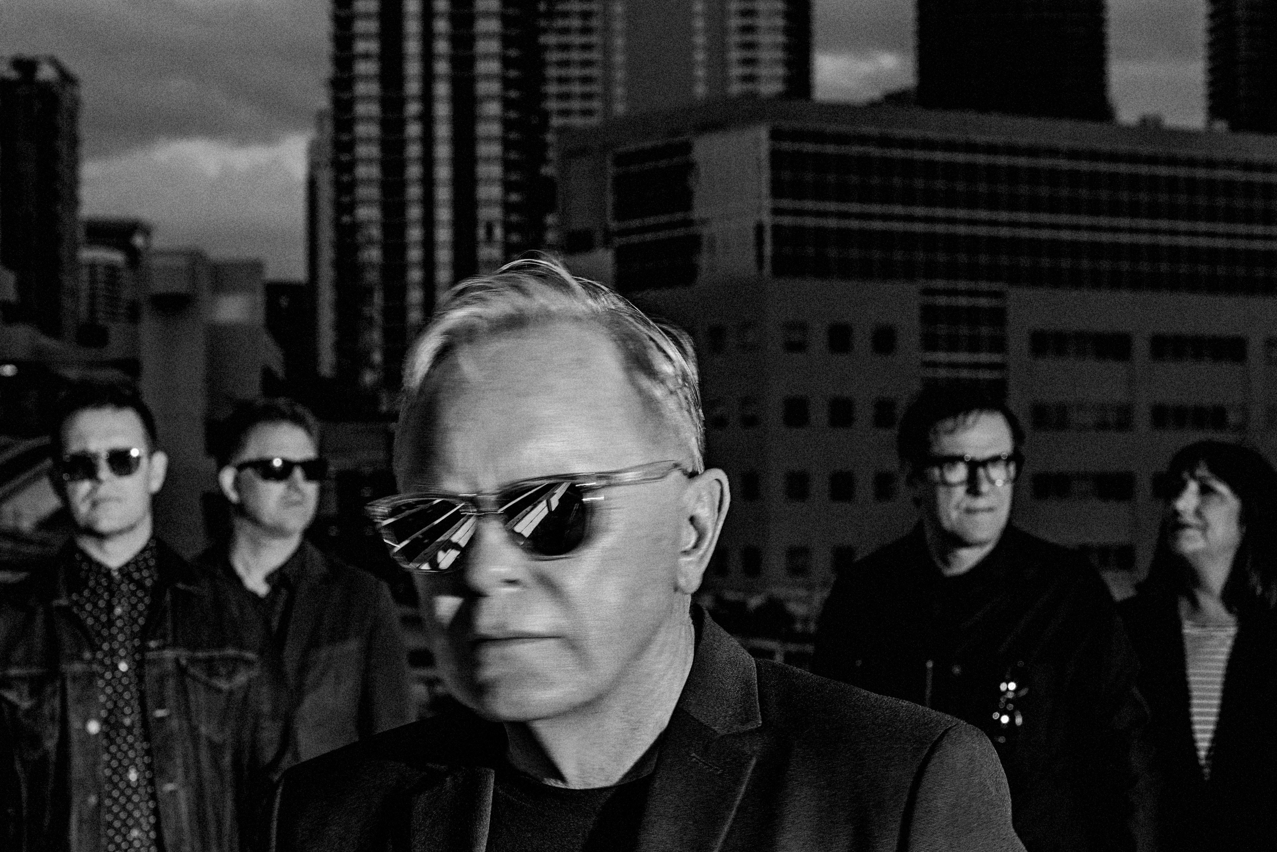 The members of New Order, standing on a building's roof, face the camera