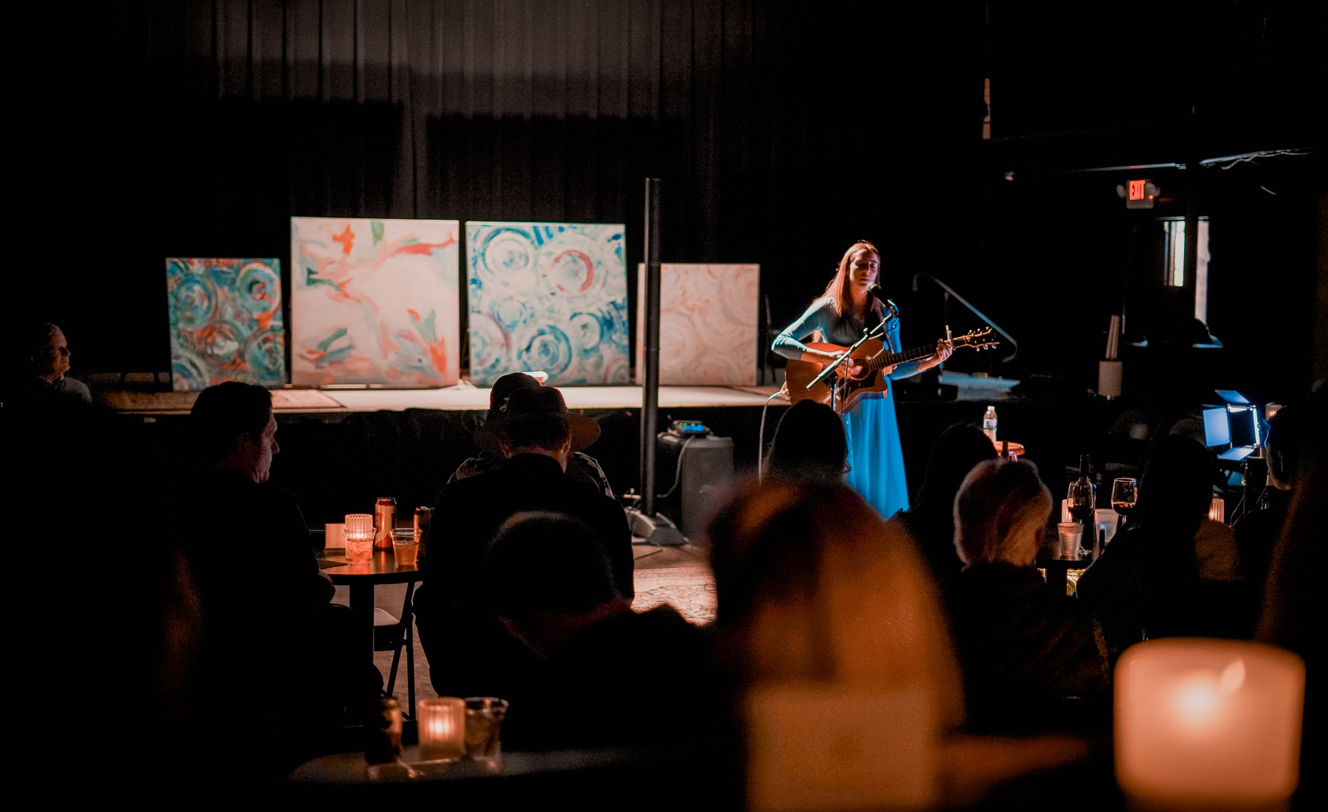 A performer singing and playing guitar in front of large canvas art pieces