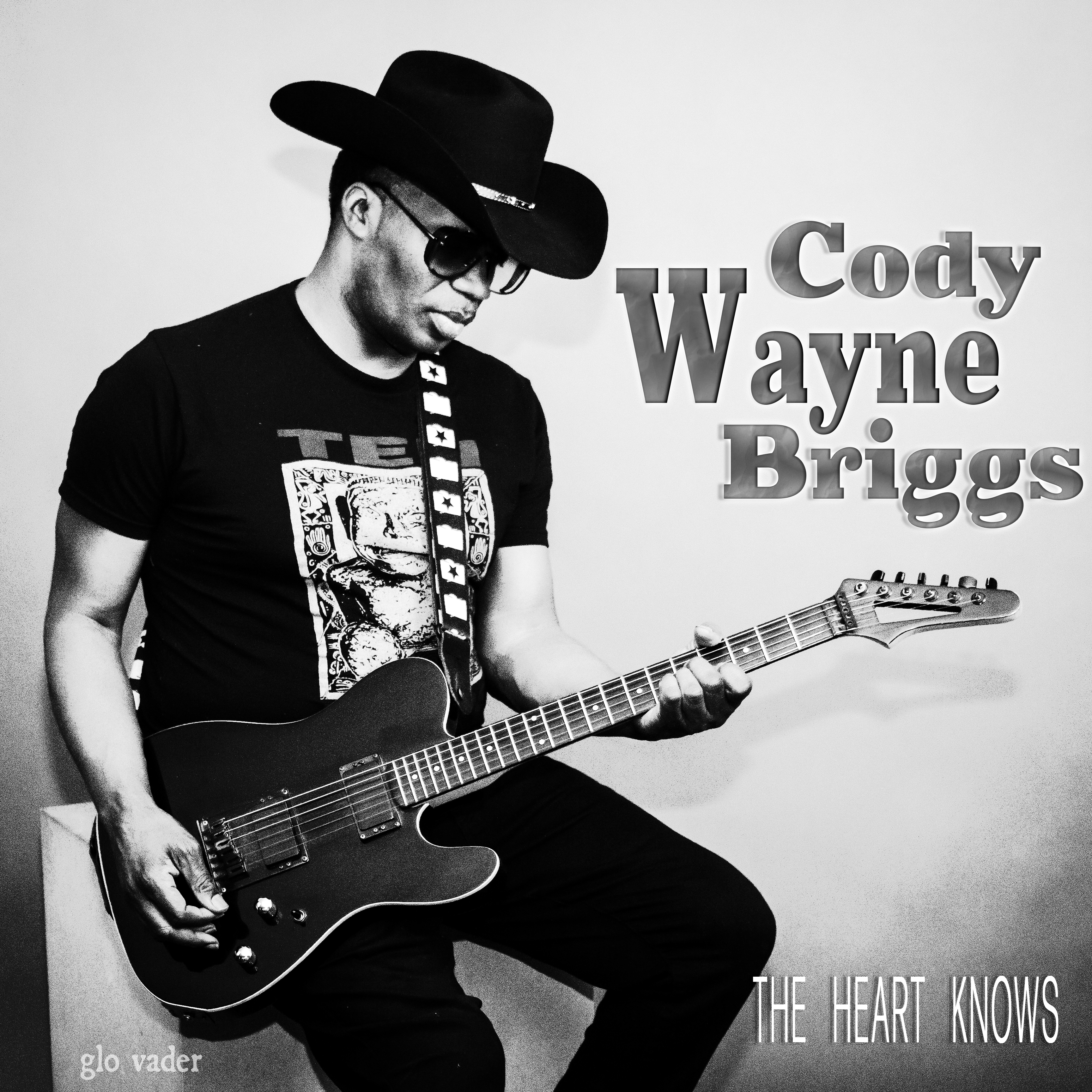 Wearing a black T-shirt and cowboy hat, Cody Lynn Briggs holds an electric guitar
