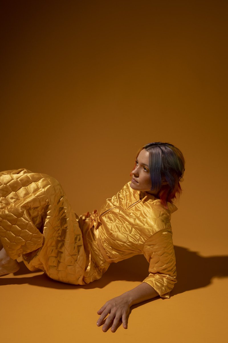 Wearing all yellow, Kaela Sinclair reclines against a yellow background