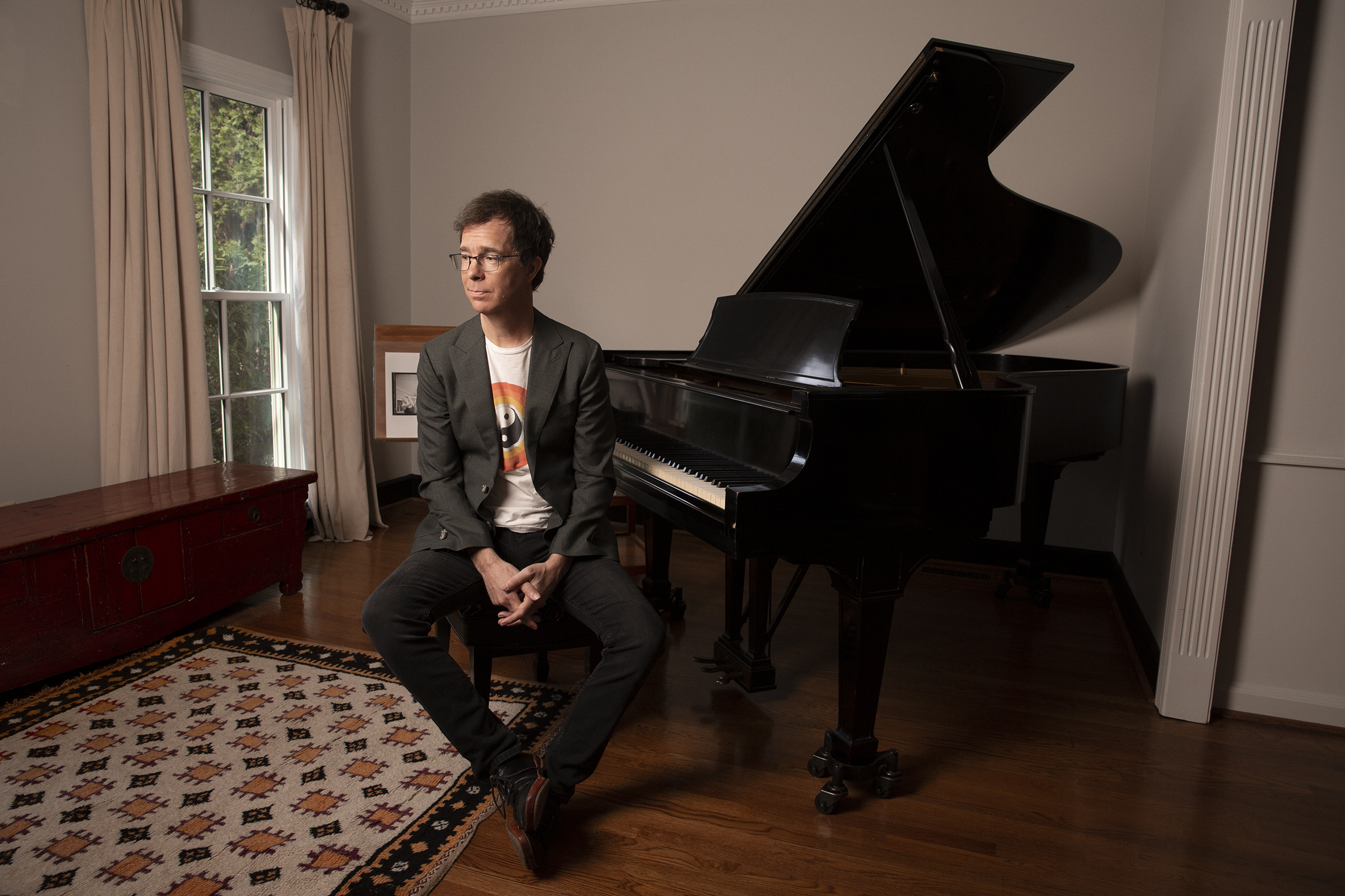 Ben Folds, wearing a jacket and a T-shirt, sits at a piano