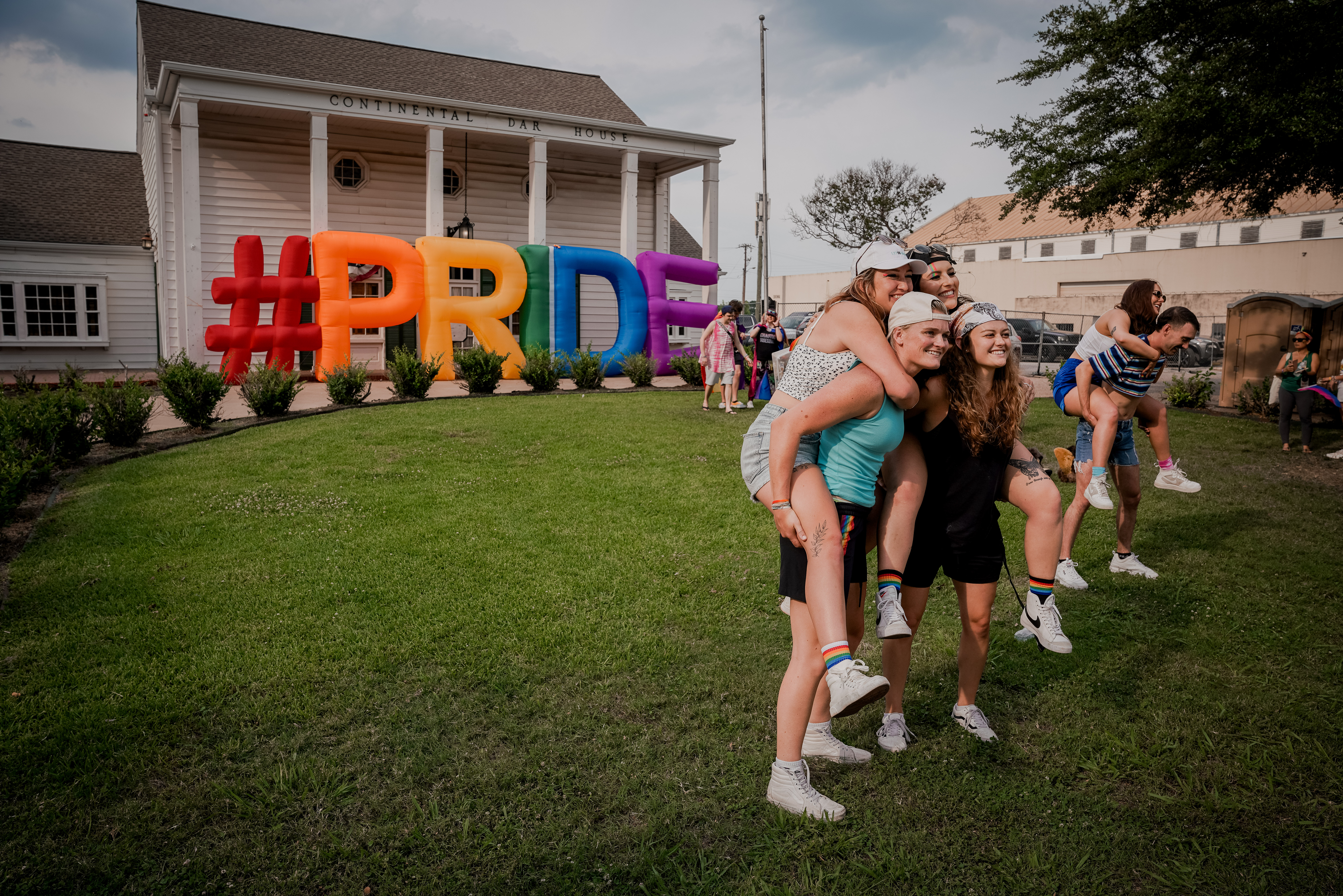 People riding piggyback for a group photo in front of a rainbow -colored inflatable that says "PRIDE"