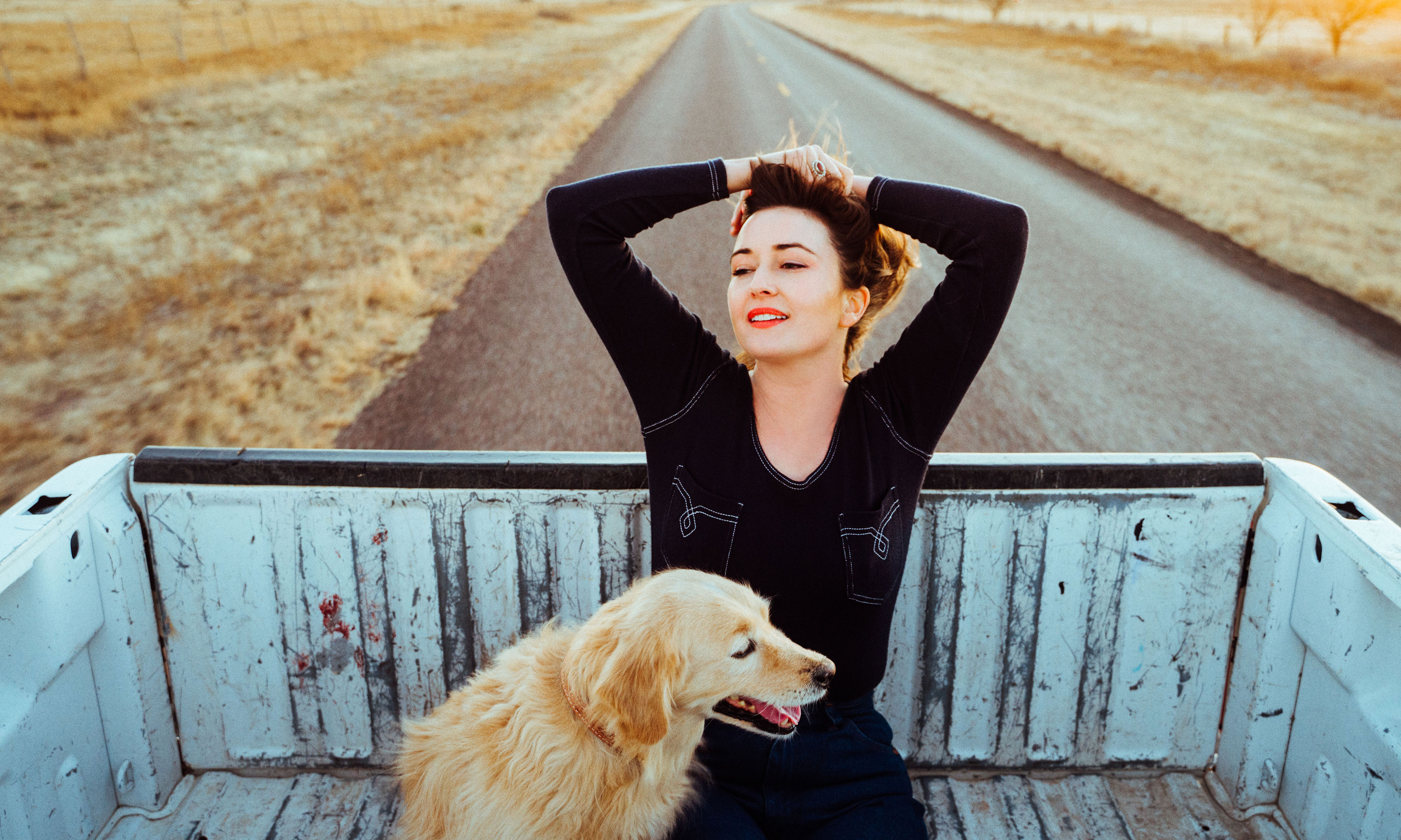 Jess Williamson reclines in the bed of a pick-up truck, with a dog in front of her.