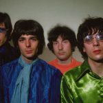 Four men wearing psychedelic clothes face the camera