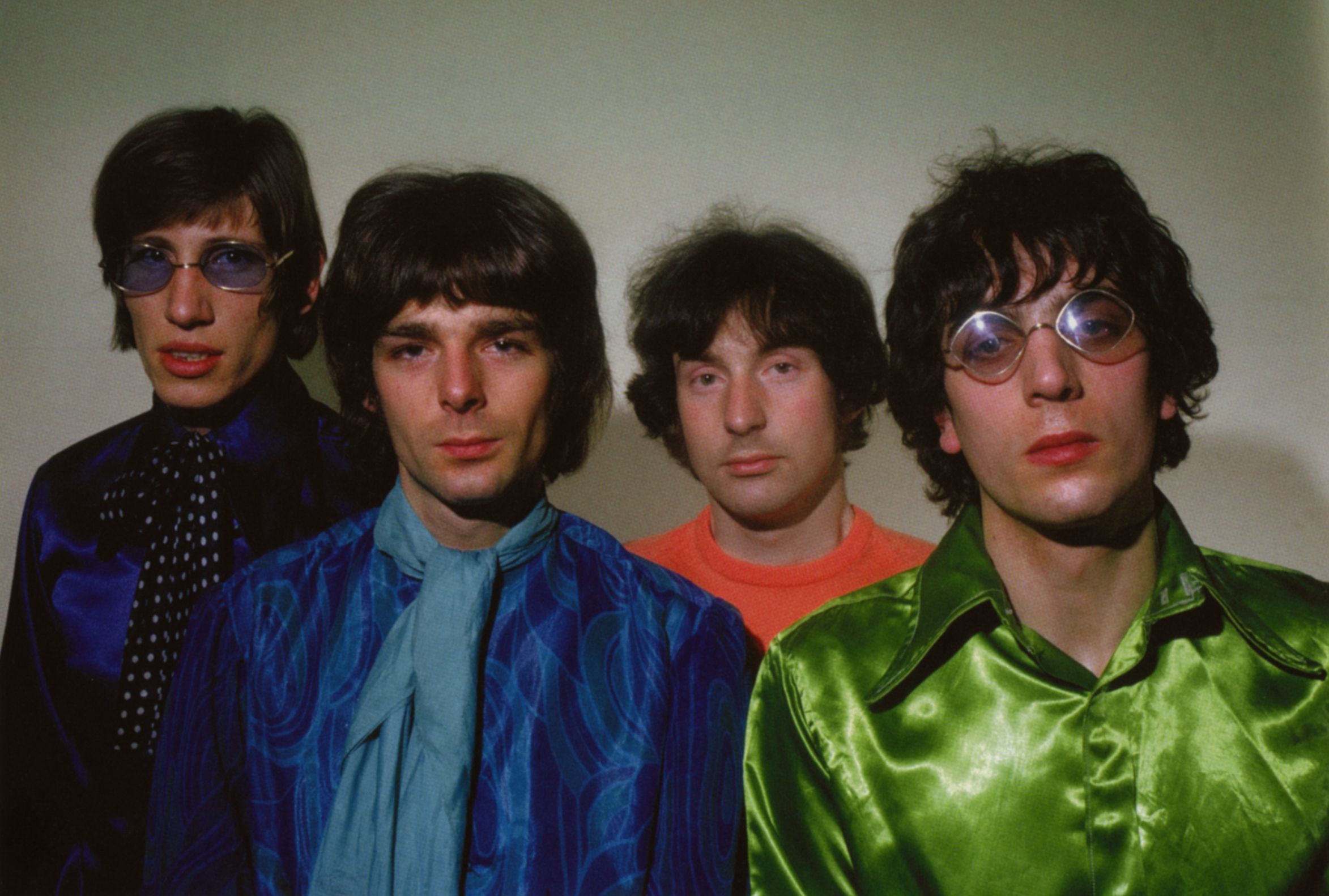 Four men wearing psychedelic clothes face the camera