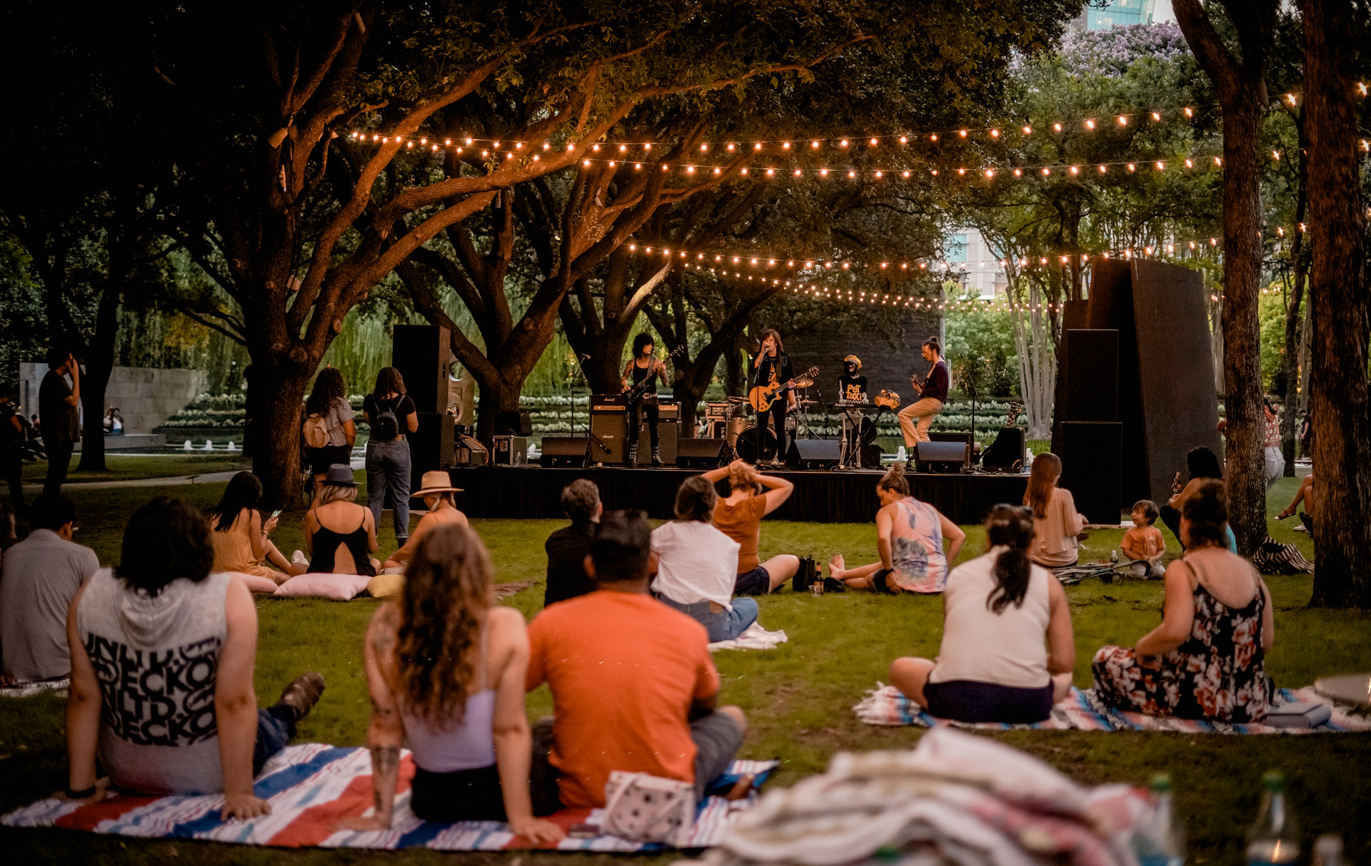 A wide shot of musicians on a stage and people sitting on blankets on grass