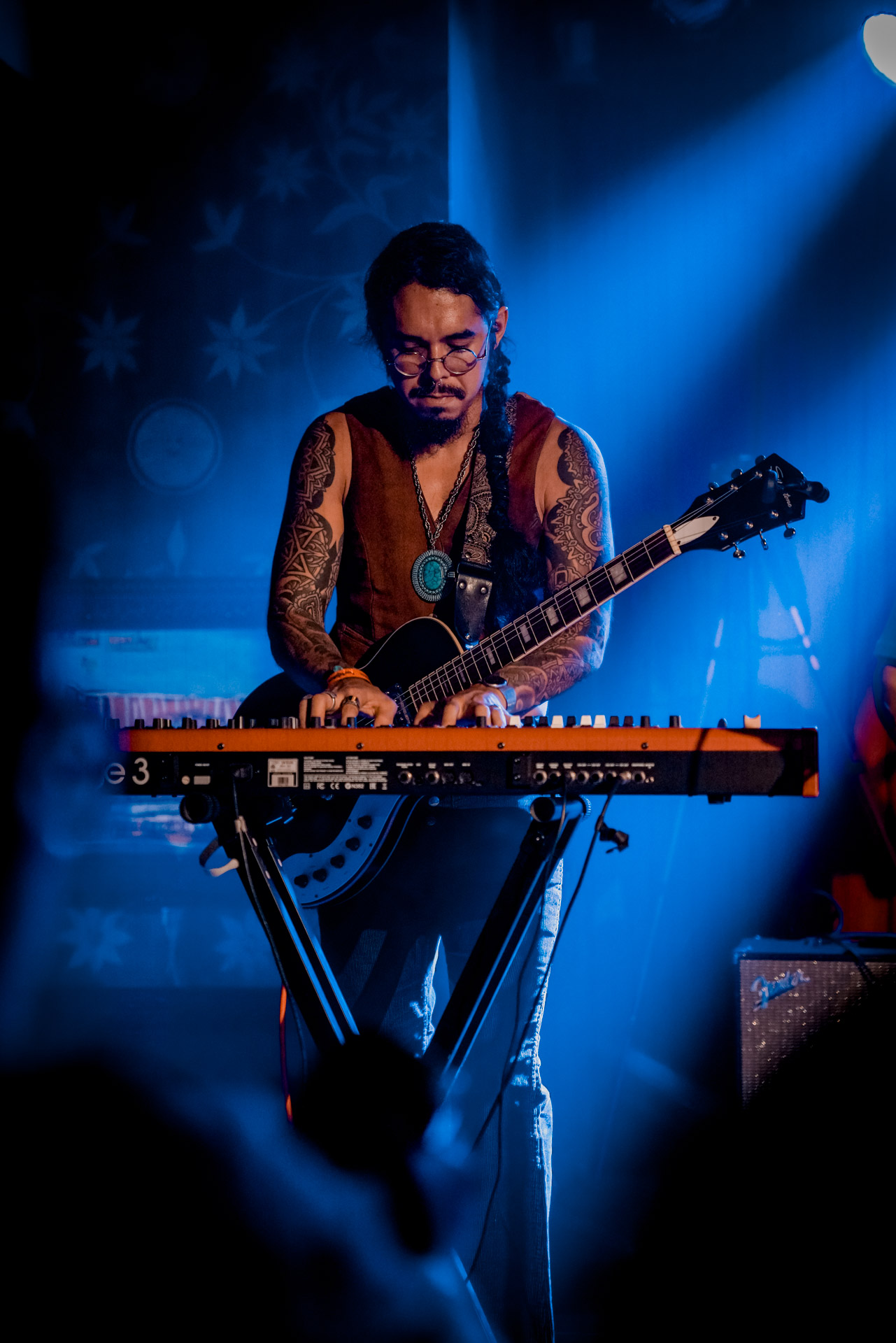 A musician playing keyboard with a guitar strapped around them