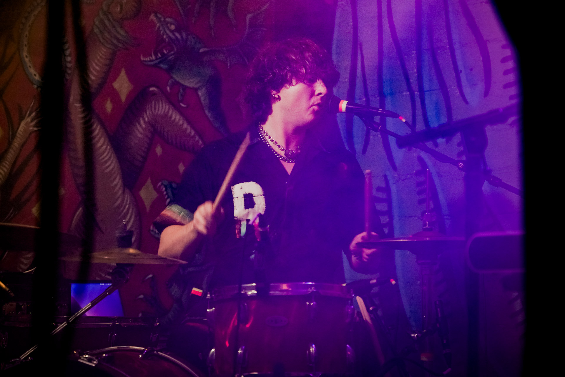 A musician on stage singing and playing drums