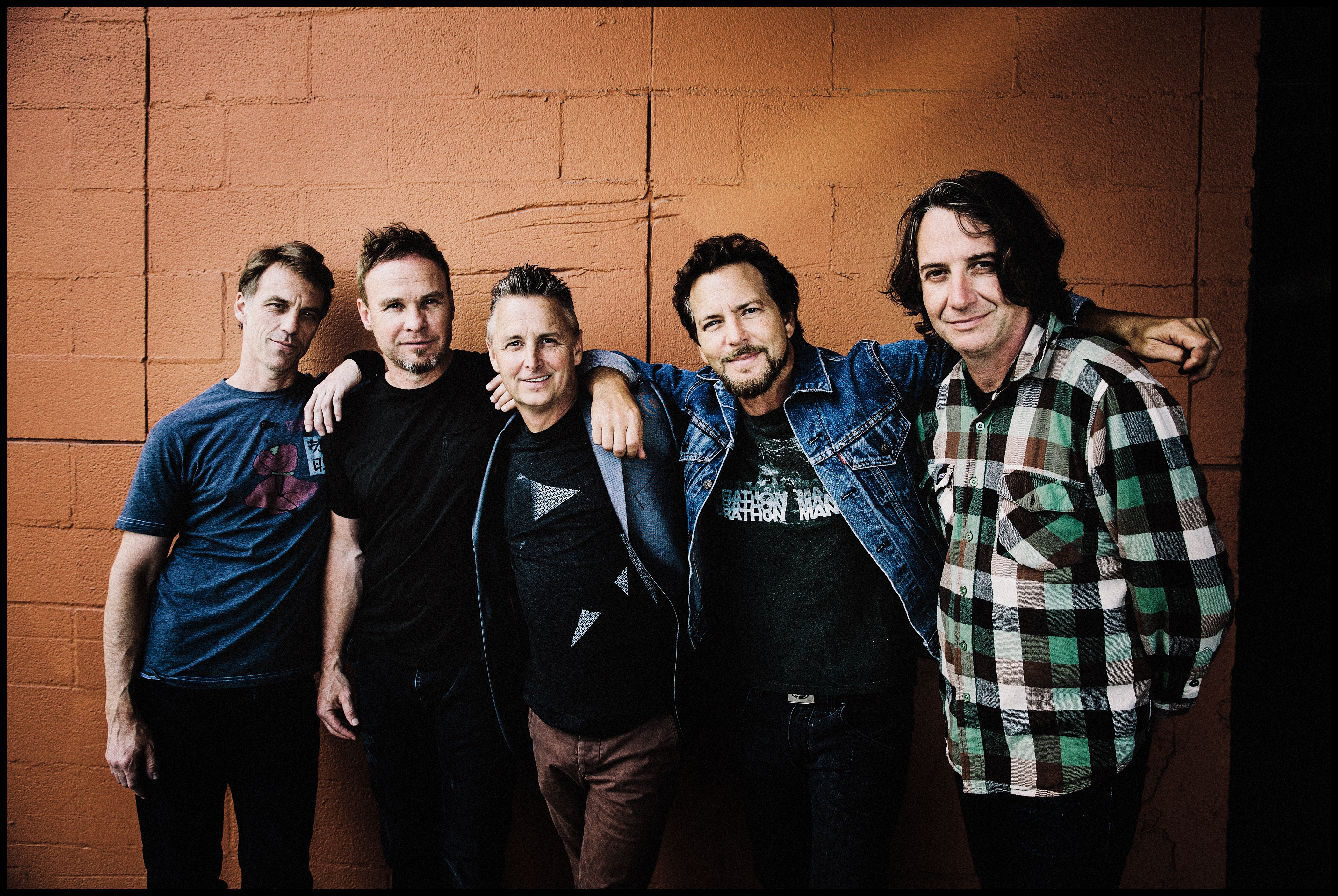 The members of Pearl Jam pose in front of a brown cinderblock wall