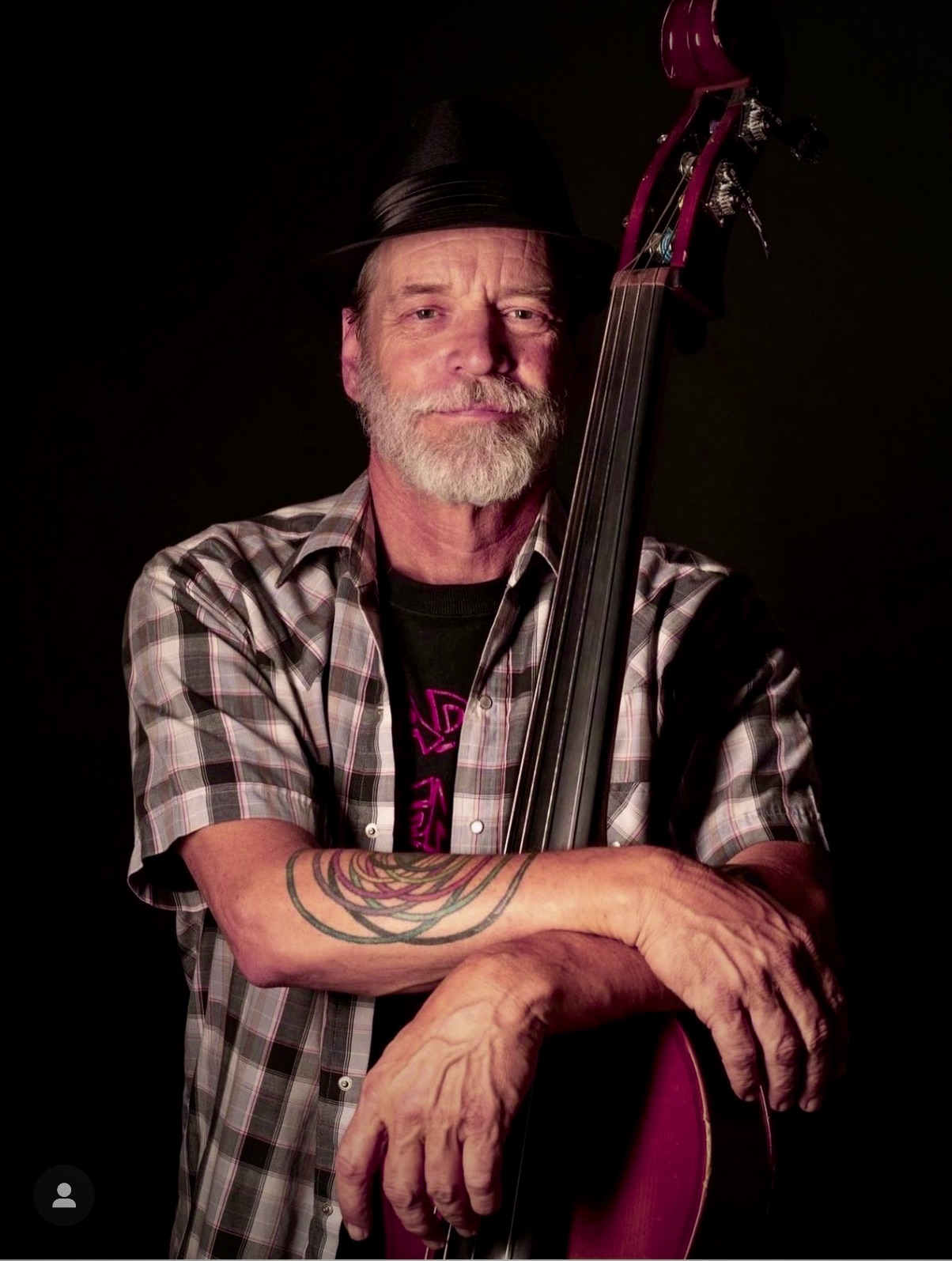 Brad Houser, standing against a black backdrop, holds a stand-up bass