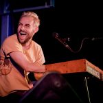 A musician playing keyboard and laughing on stage