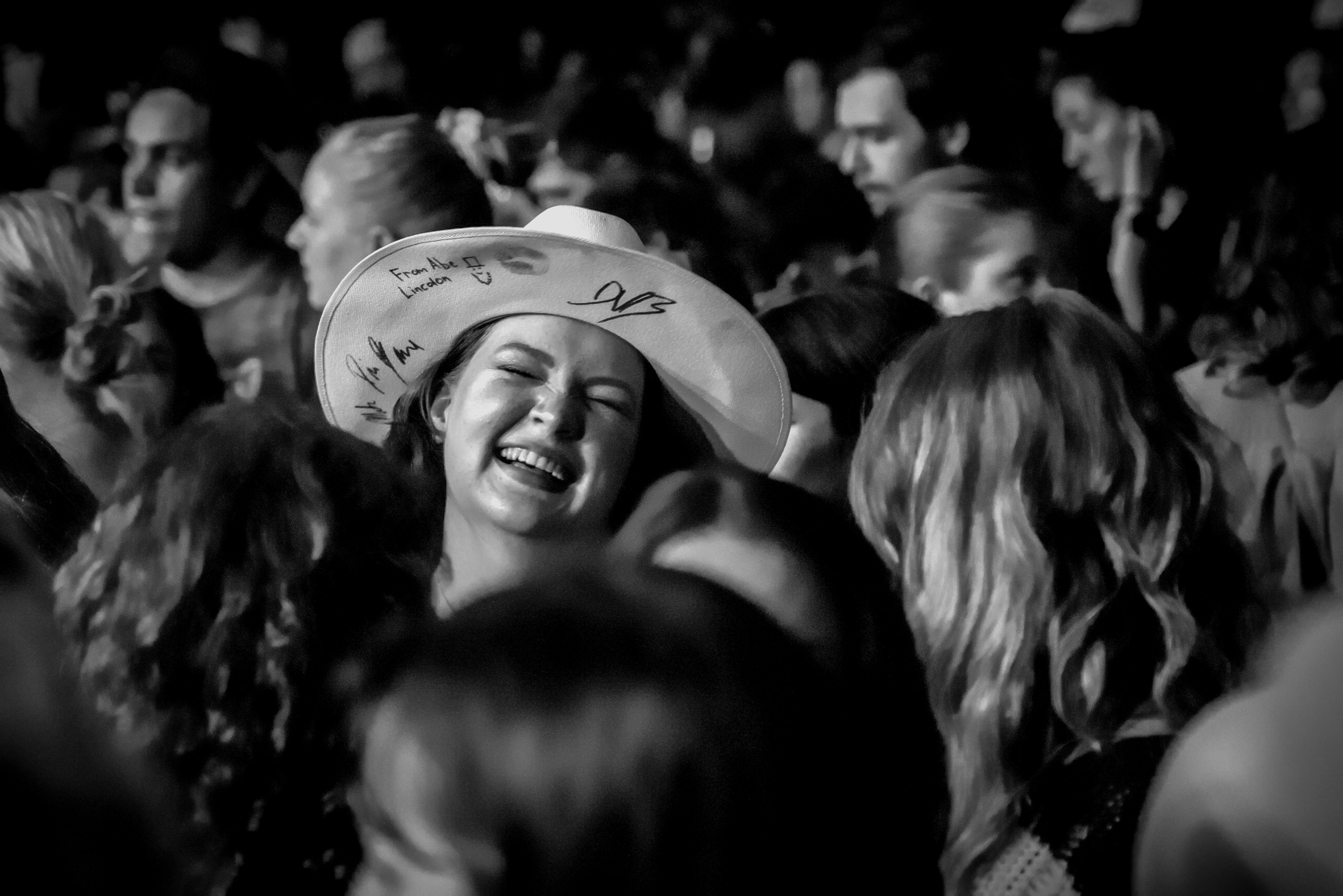 A person in the crowd smiling with a signed hat on 