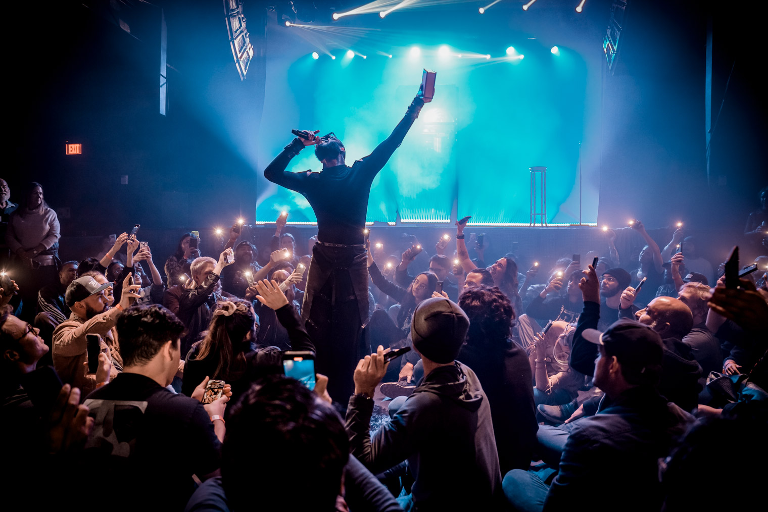 A singer surrounded by an audience sitting on the floor with their phone lights lit
