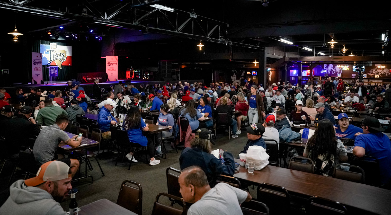 A wide shot of over a hundred people sittign at tables in front of a stage