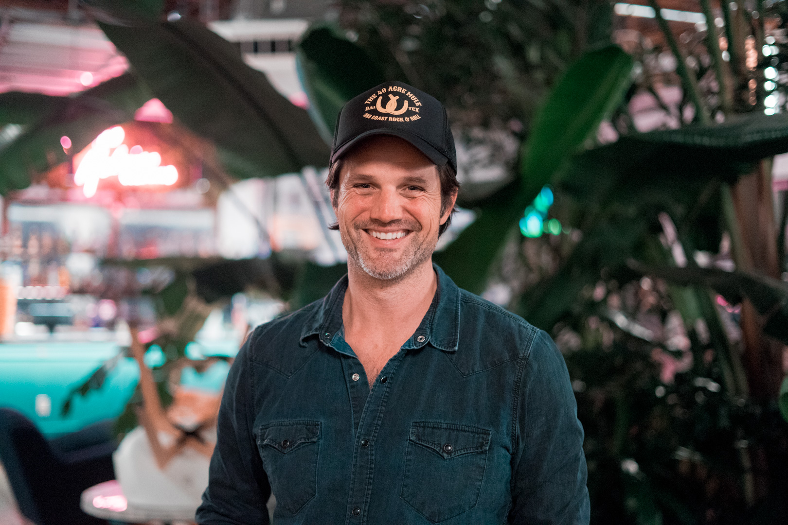 A man smiling into camera wearing a baseball hat 