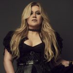 Kelly Clarkson, wearing a black dress, stares into the camera