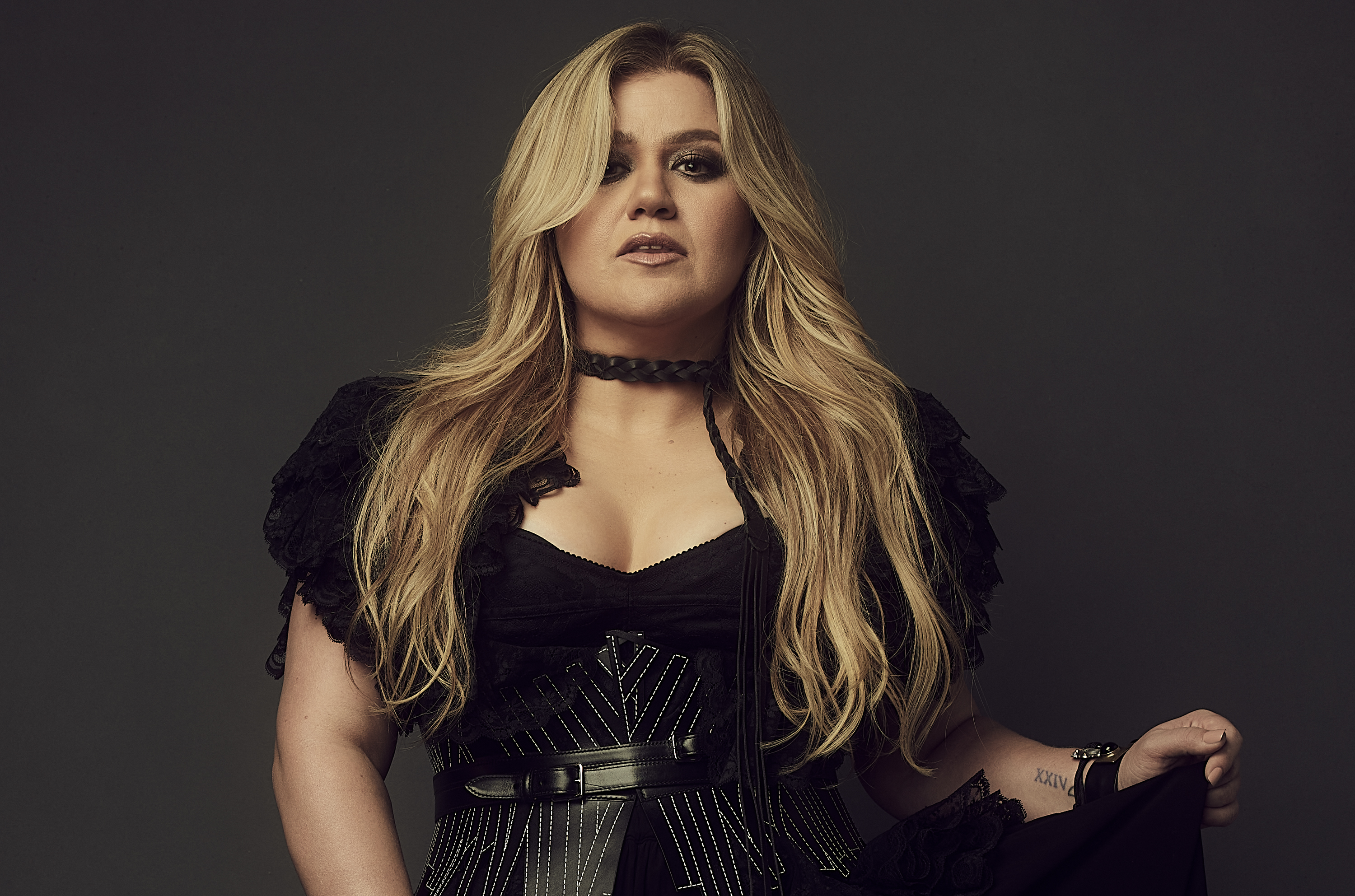 Kelly Clarkson, wearing a black dress, stares into the camera