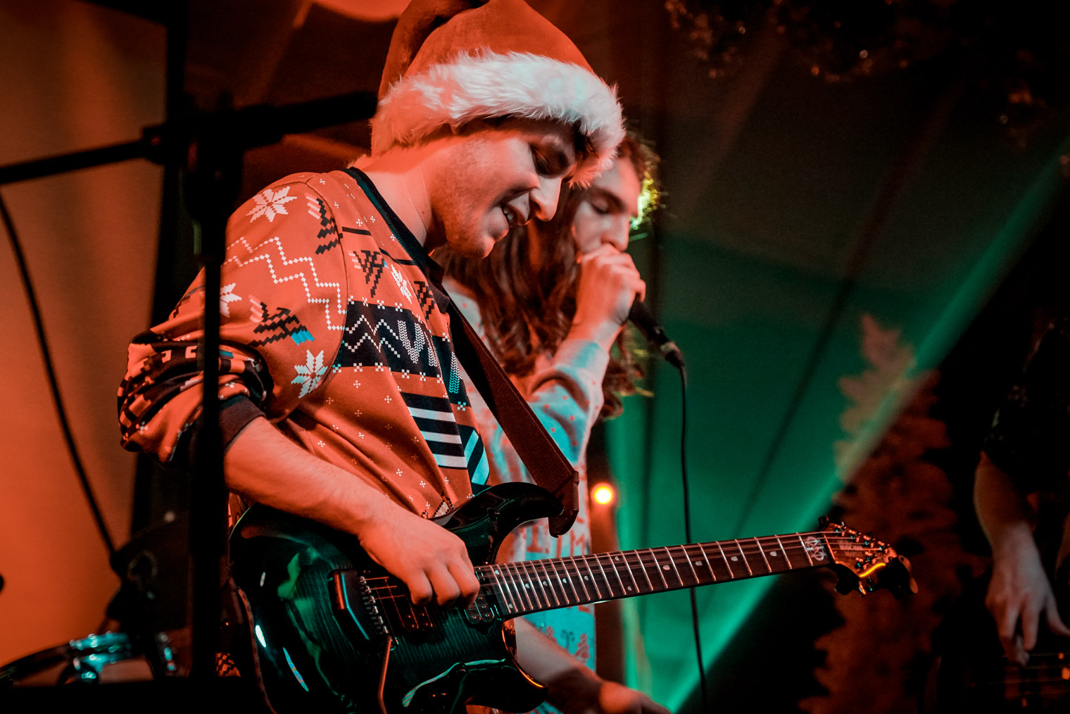 A musician playing guitar on stage wearing a Santa hat