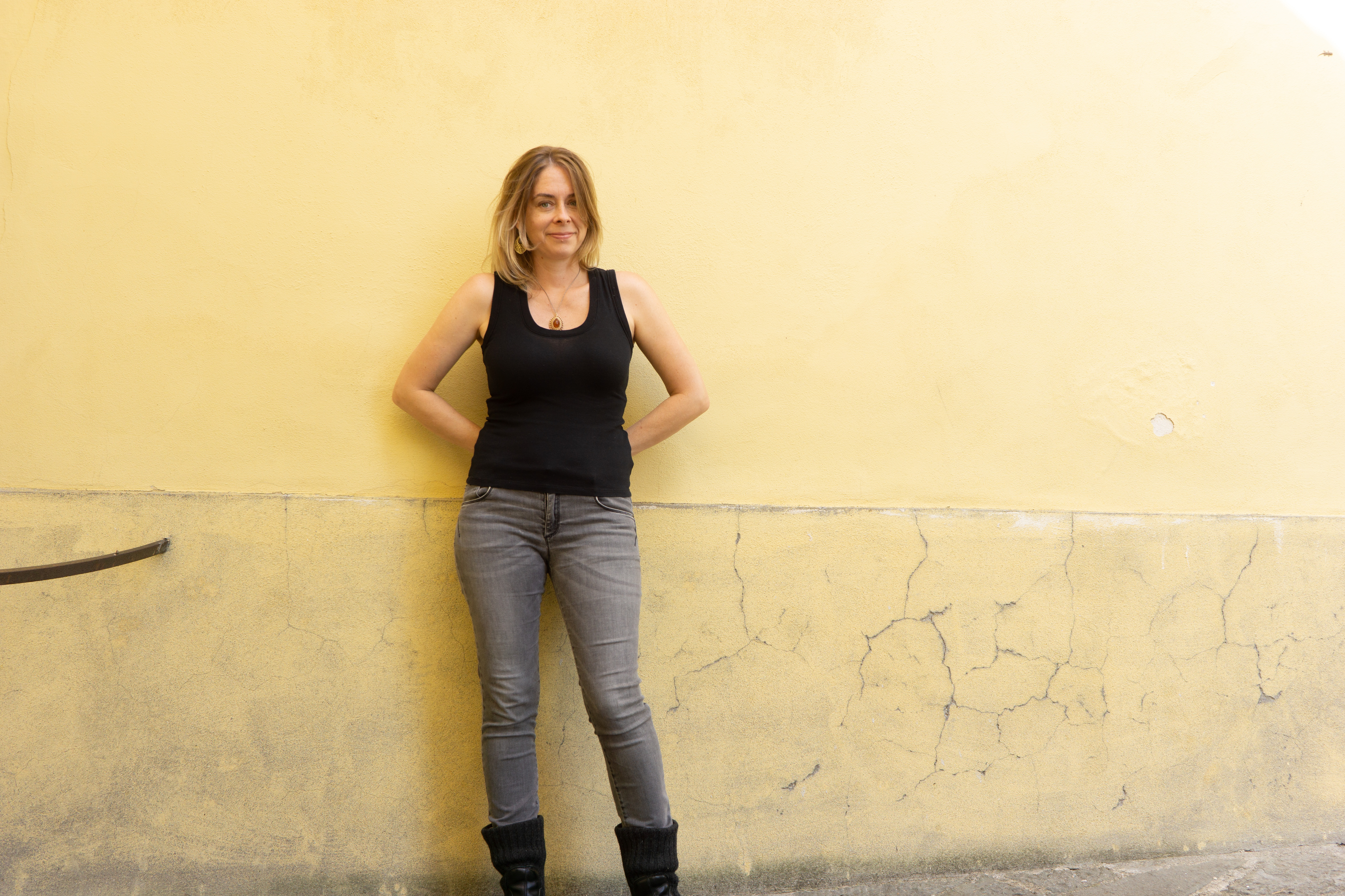 Vanessa Peters, in a black shirt and gray pants, stands against a light yellow wall