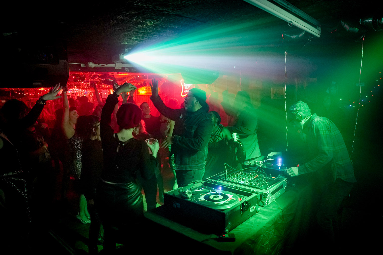 A room full of people dancing with a DJ on turntables