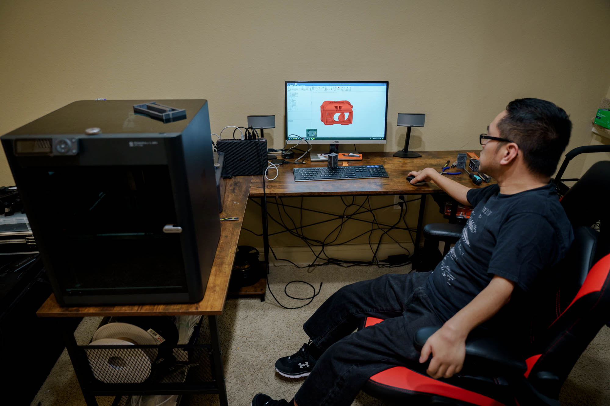A musican sitting at a desk with a 3D printer and computer