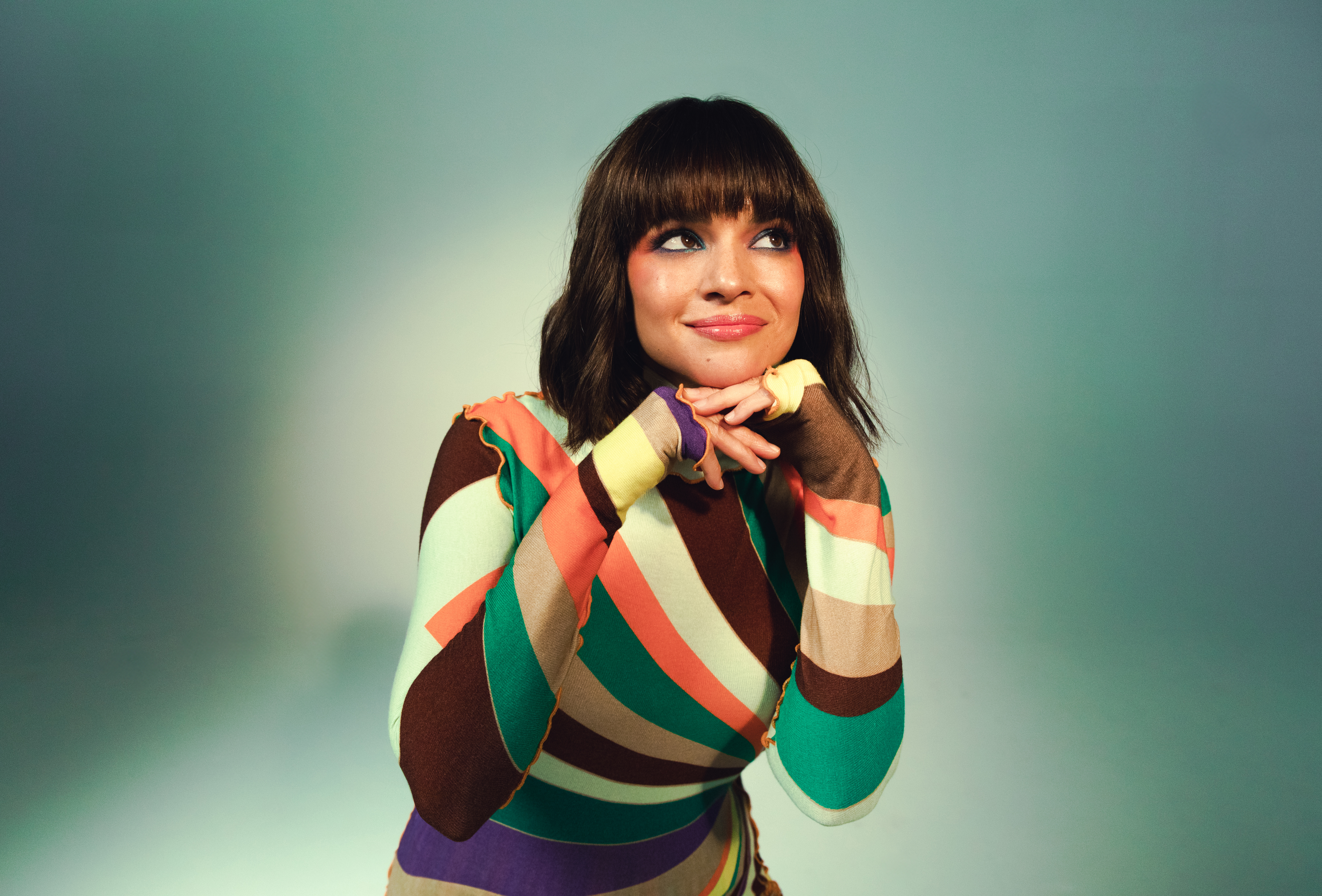 Wearing a colorful striped dress, Norah Jones poses against a white backdrop