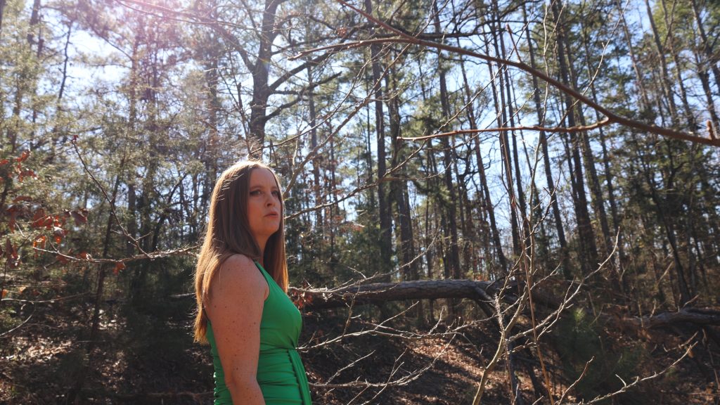 A woman wearing green stands in a forest