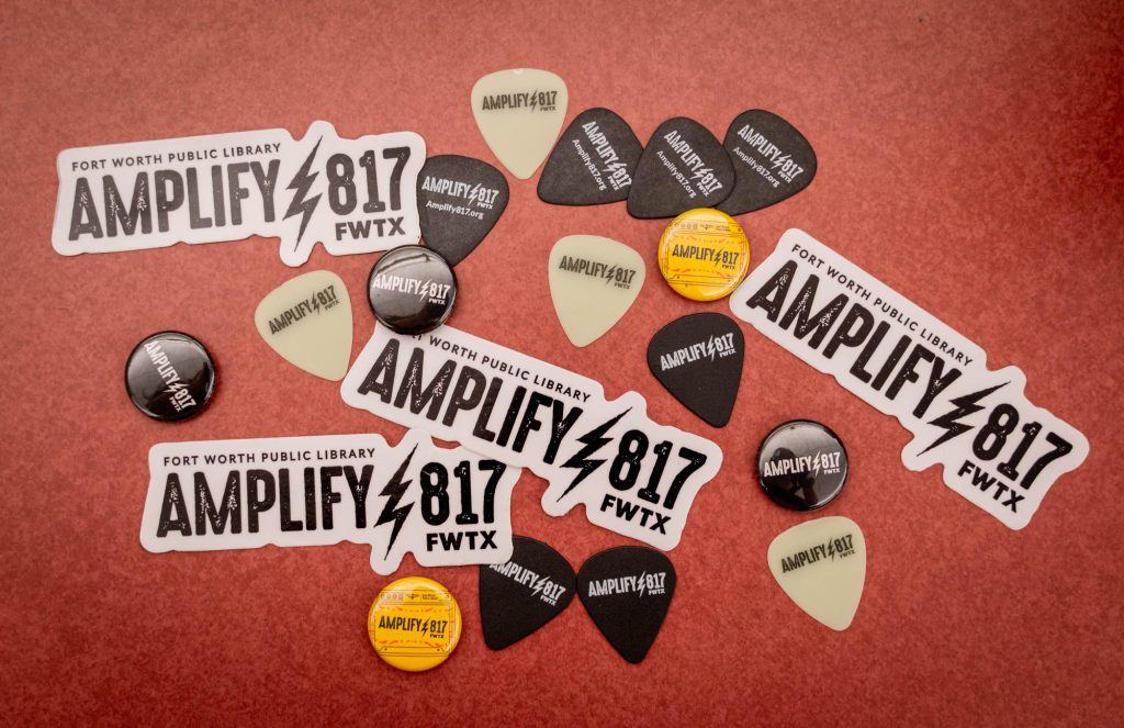 An assortment of "Amplify 817" stickers, buttons and guitar picks